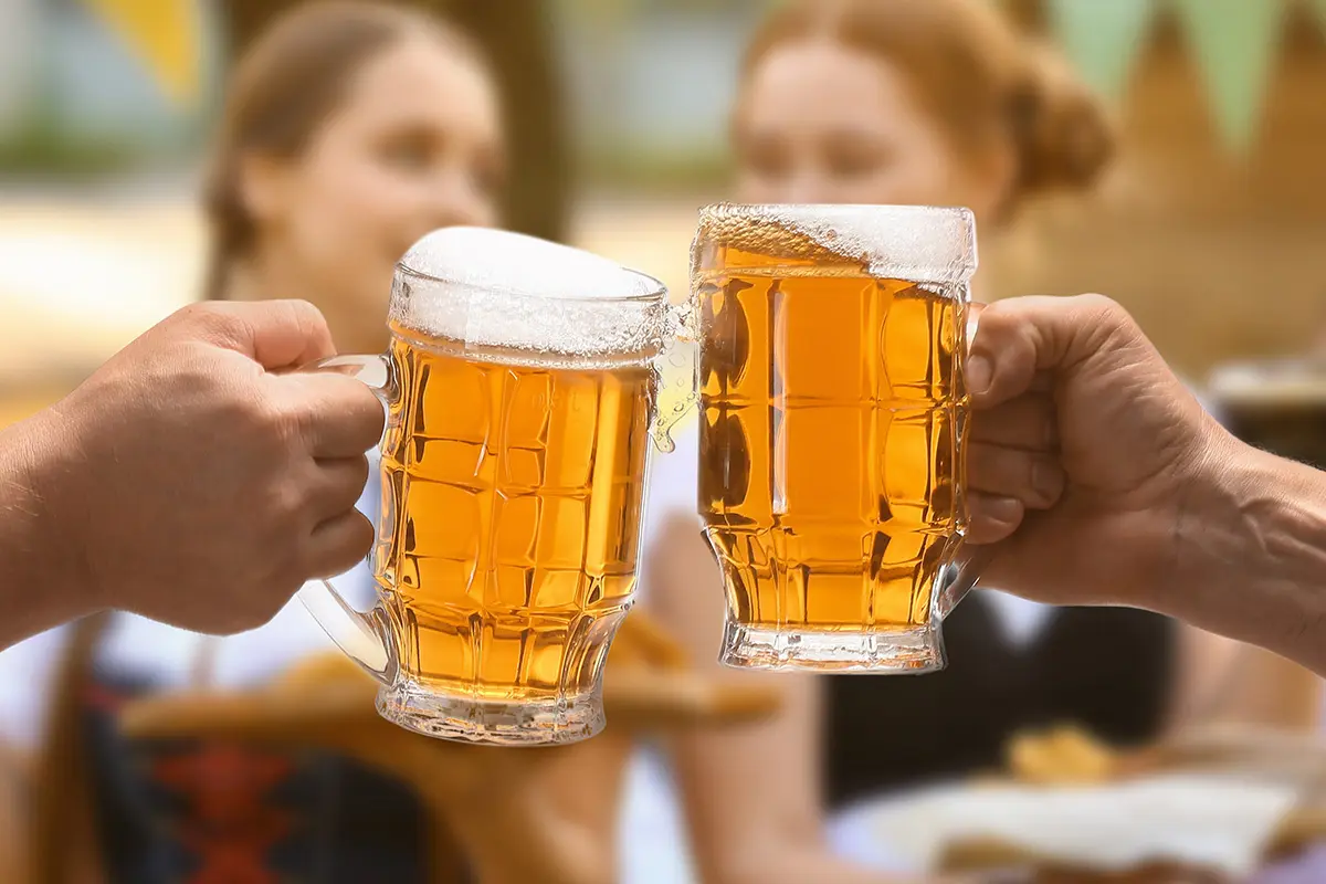 Two steins of golden lager clinking together in celebration, highlighting Oktoberfest and Freshers Week drinks deals.
