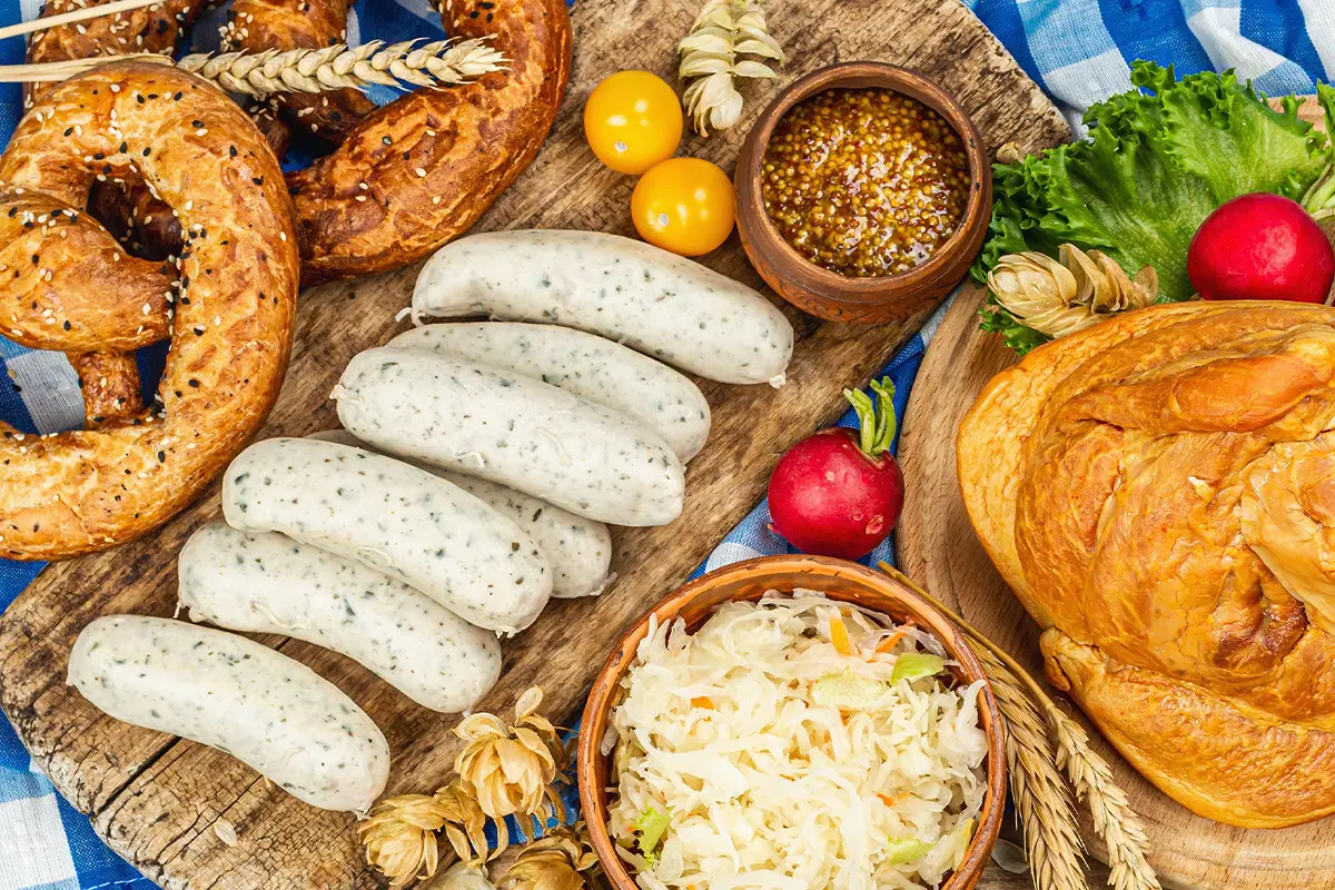 Traditional Bavarian feast with Weißwurst sausages, fresh pretzels, sauerkraut, mustard, and bread on a rustic wooden board — perfect for pairing with Oktoberfest and Freshers Week drinks deals from Bargain Booze.