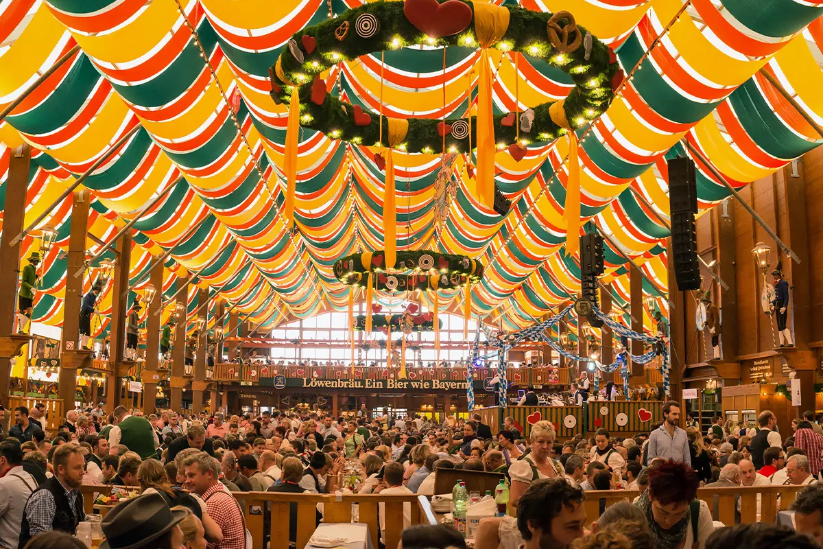 Crowds enjoying beer and food inside a decorated festival tent, celebrating with Oktoberfest and Freshers Week drinks deals.