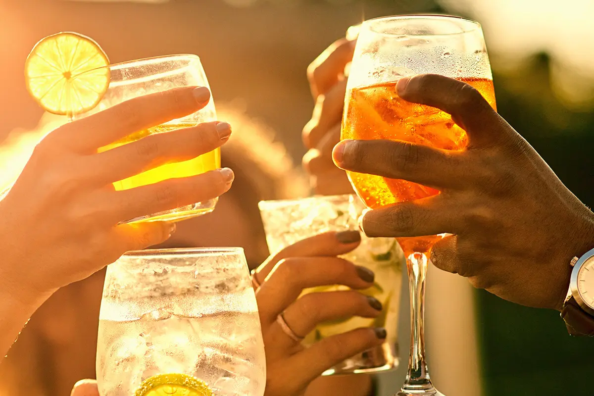 Friends raising colourful cocktails in the sunshine, celebrating with summer drinks deals.