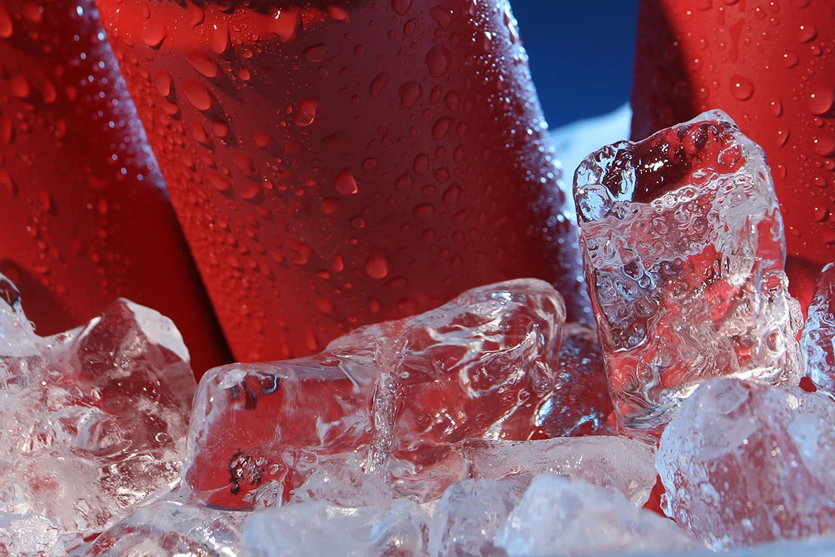Close-up of red drink cans surrounded by ice cubes, symbolising early Christmas drinks deals and festive gifting available chilled at Bargain Booze.