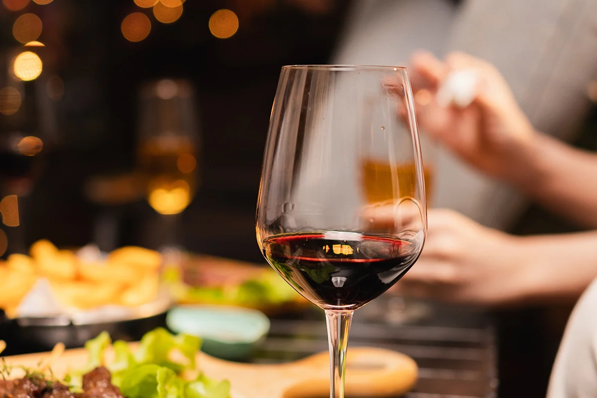 A glass of red wine on a cosy table with warm lights and festive food, reflecting early Christmas drinks deals and festive gifting at Bargain Booze.