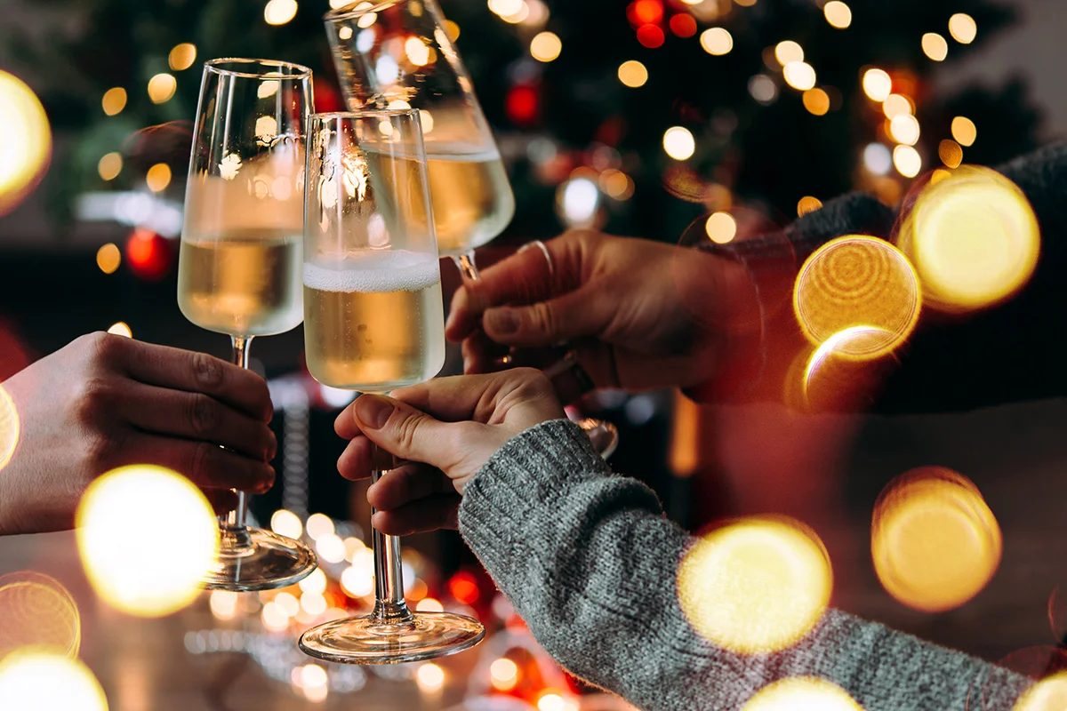 Friends raising champagne glasses in a festive toast with twinkling Christmas lights, celebrating early Christmas drinks deals and festive gifting from Bargain Booze.