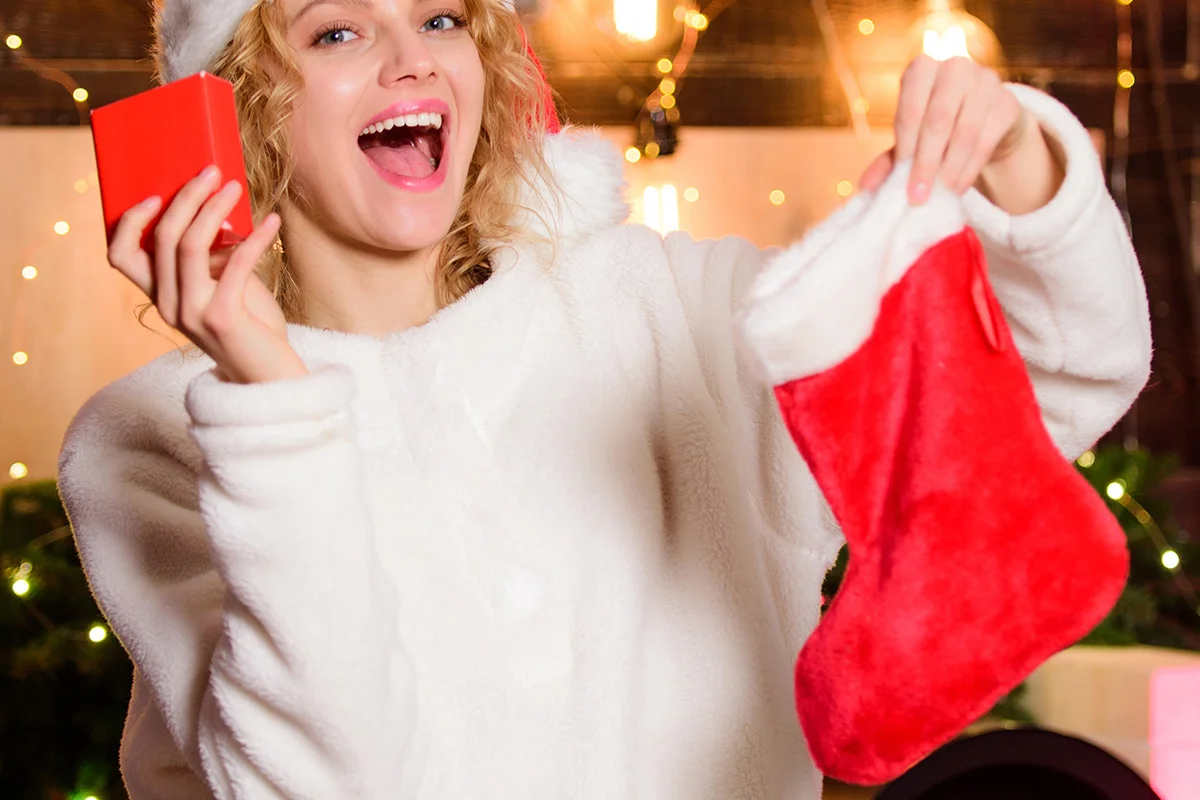 A woman in a Santa hat smiling and holding a Christmas stocking and small gift, celebrating early Christmas drinks deals and festive gifting from Bargain Booze.