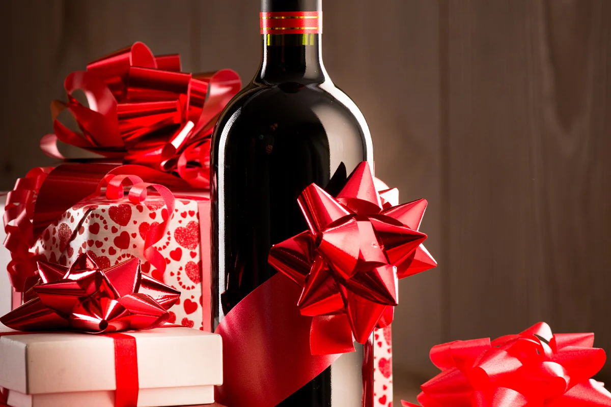 A bottle of red wine wrapped with a festive bow surrounded by gift boxes, celebrating early Christmas drinks deals and festive gifting at Bargain Booze.