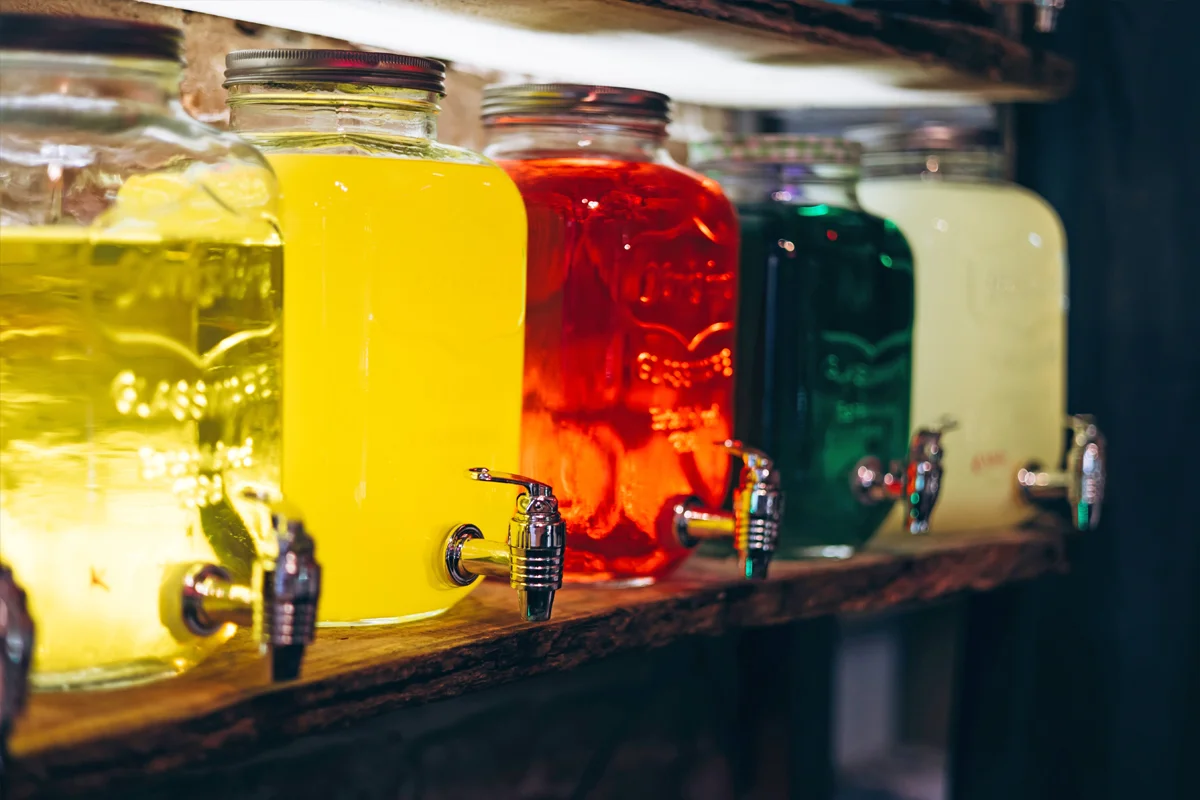 A row of large glass dispensers filled with brightly coloured drinks, each with a chrome tap.