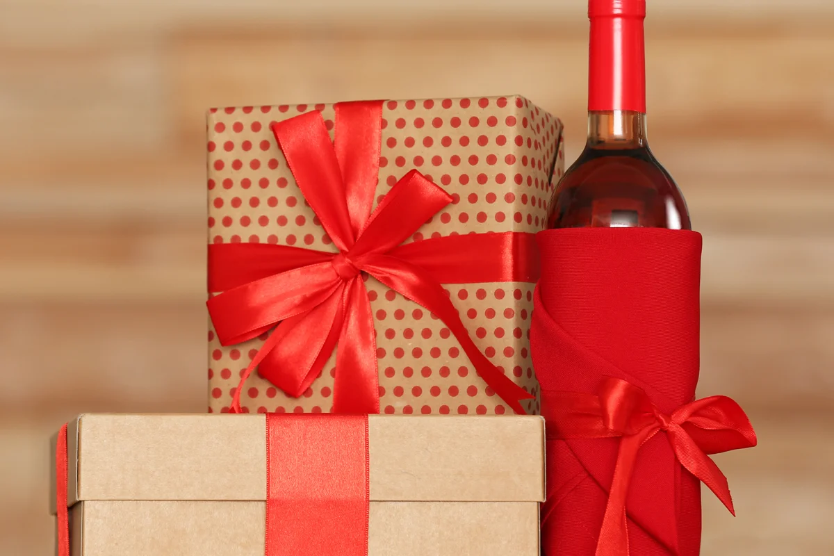 A collection of Christmas gifts wrapped in red and kraft paper, alongside a wine bottle wrapped in red fabric.