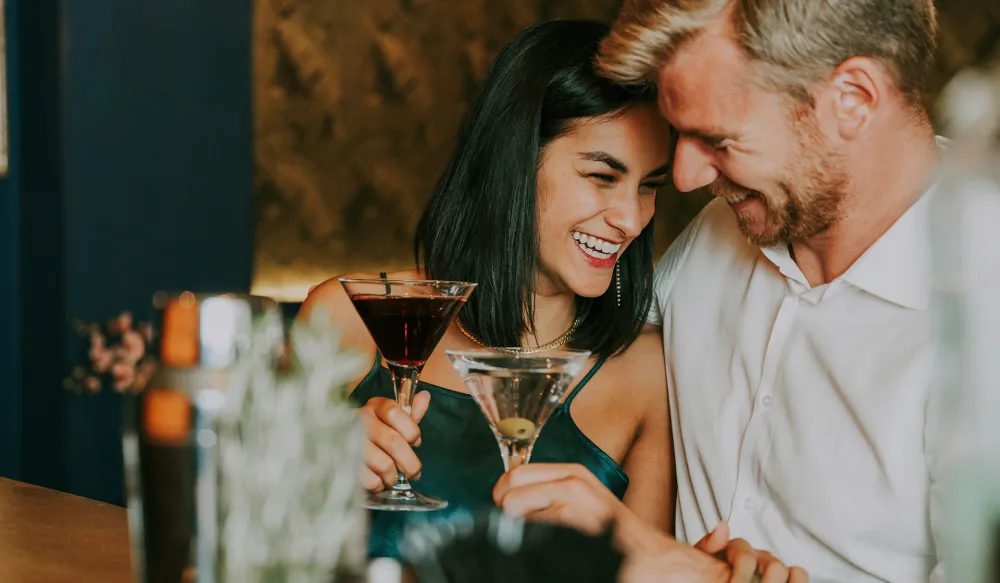 Couple smiling and enjoying cocktails together at a bar