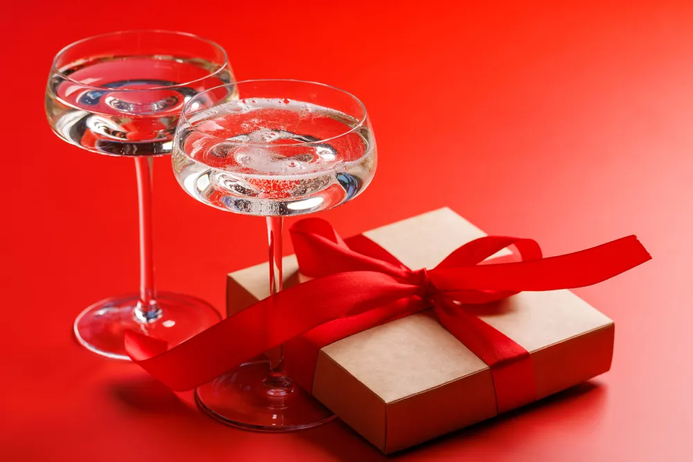 Two cocktail glasses with a gift box tied with a red ribbon