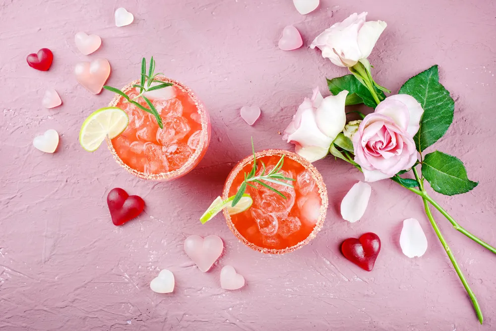 Pink cocktails with ice, citrus garnish and roses on a Valentine’s background