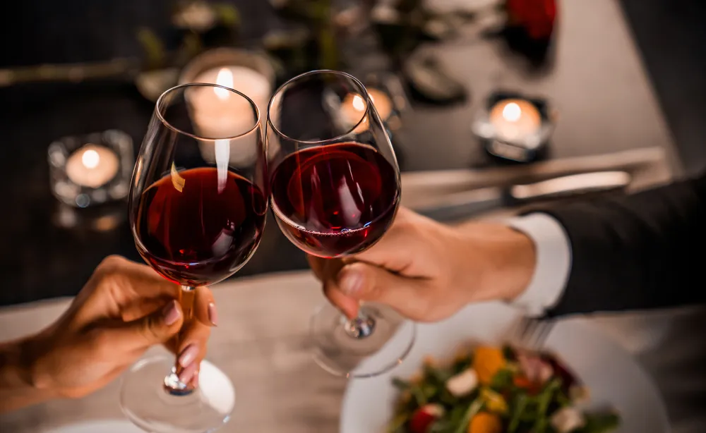 Two people toasting with glasses of red wine over dinner