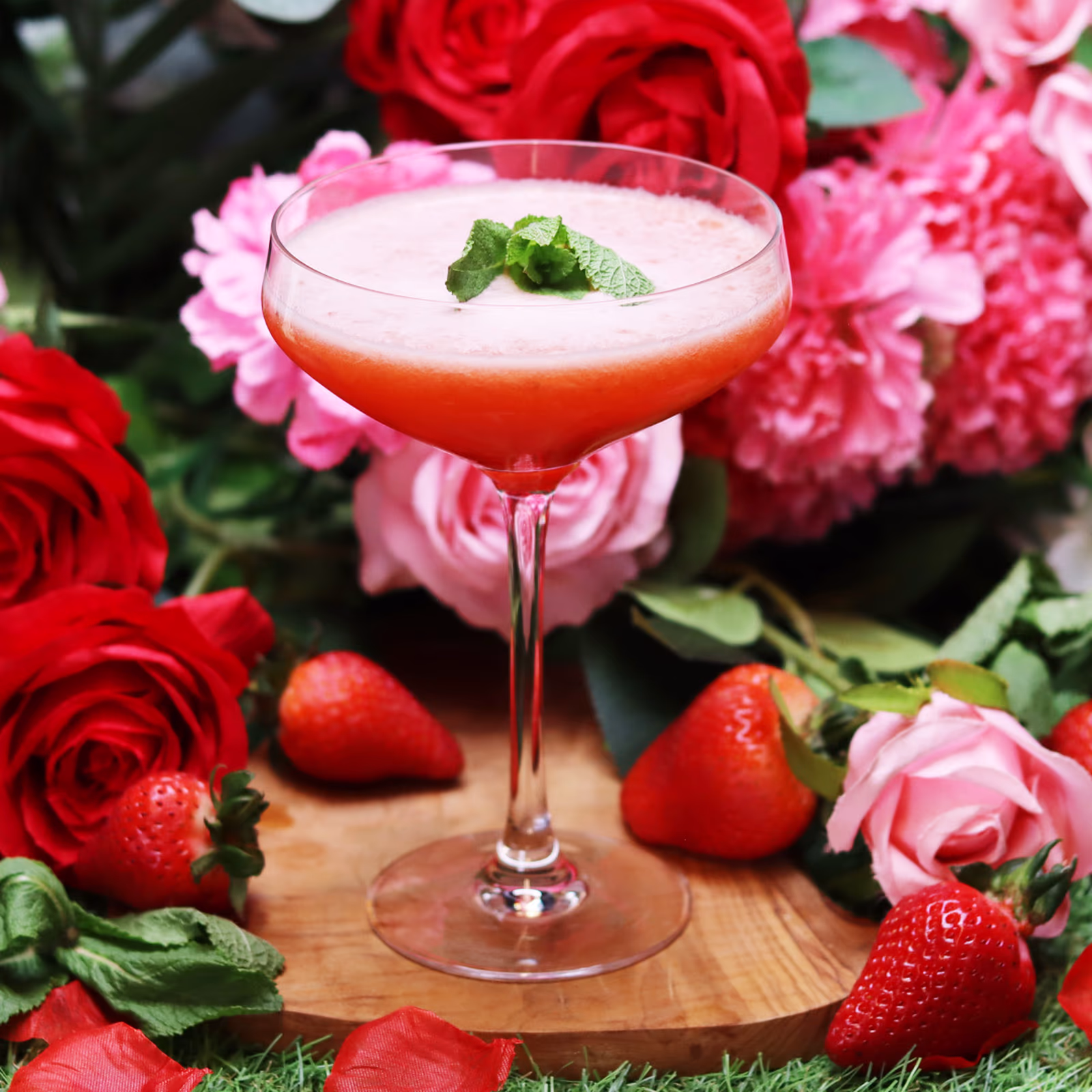 Stoli Strawberry Kiss cocktail in a coupe glass with mint garnish, fresh strawberries and roses, the Cocktail of the Month in Bargain Booze's bank holiday booze deals.